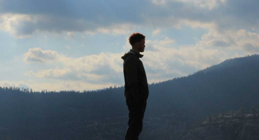 A person looks out over a mountainous landscape covered in evergreen trees. 